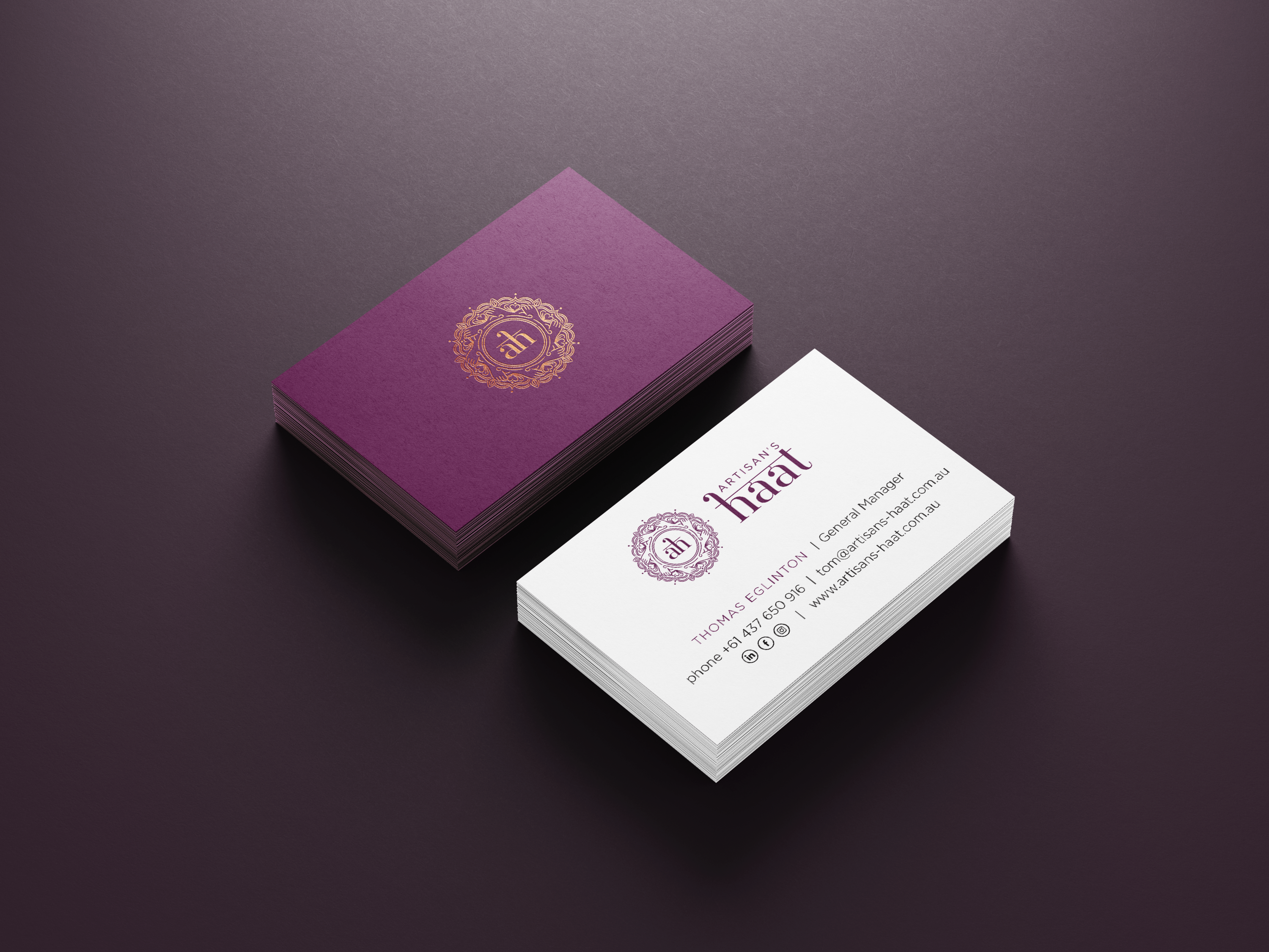 A stack of business cards on a dark purple surface. The top card in the left stack features a gold ornate logo on a purple background, while the card on the right shows "THOMAS GREEN," his title, company name, and contact details on a white background.