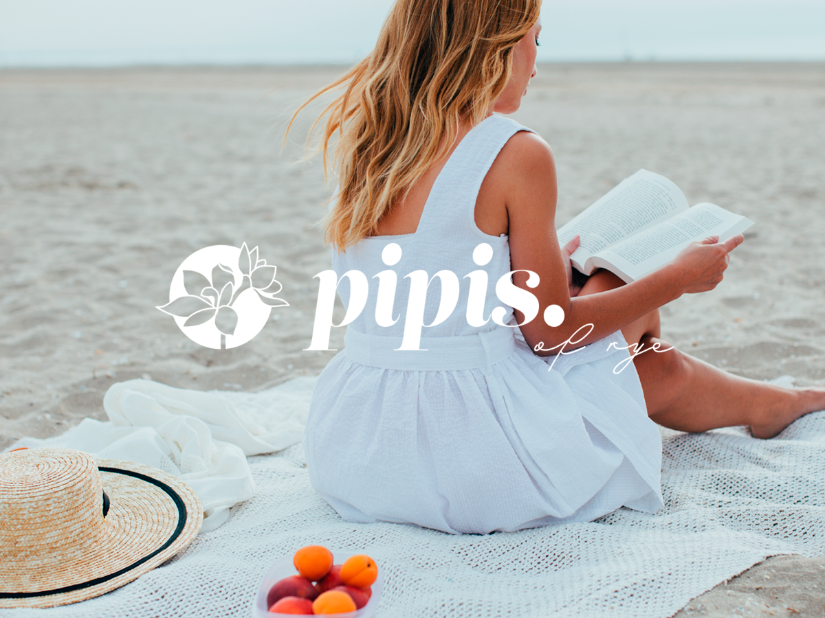 A woman with long hair sits on a white blanket at the beach, reading a book. She is wearing a sleeveless white dress. A straw hat and a bowl of apricots are beside her. The words "pipis of rye" are overlaid on the image.