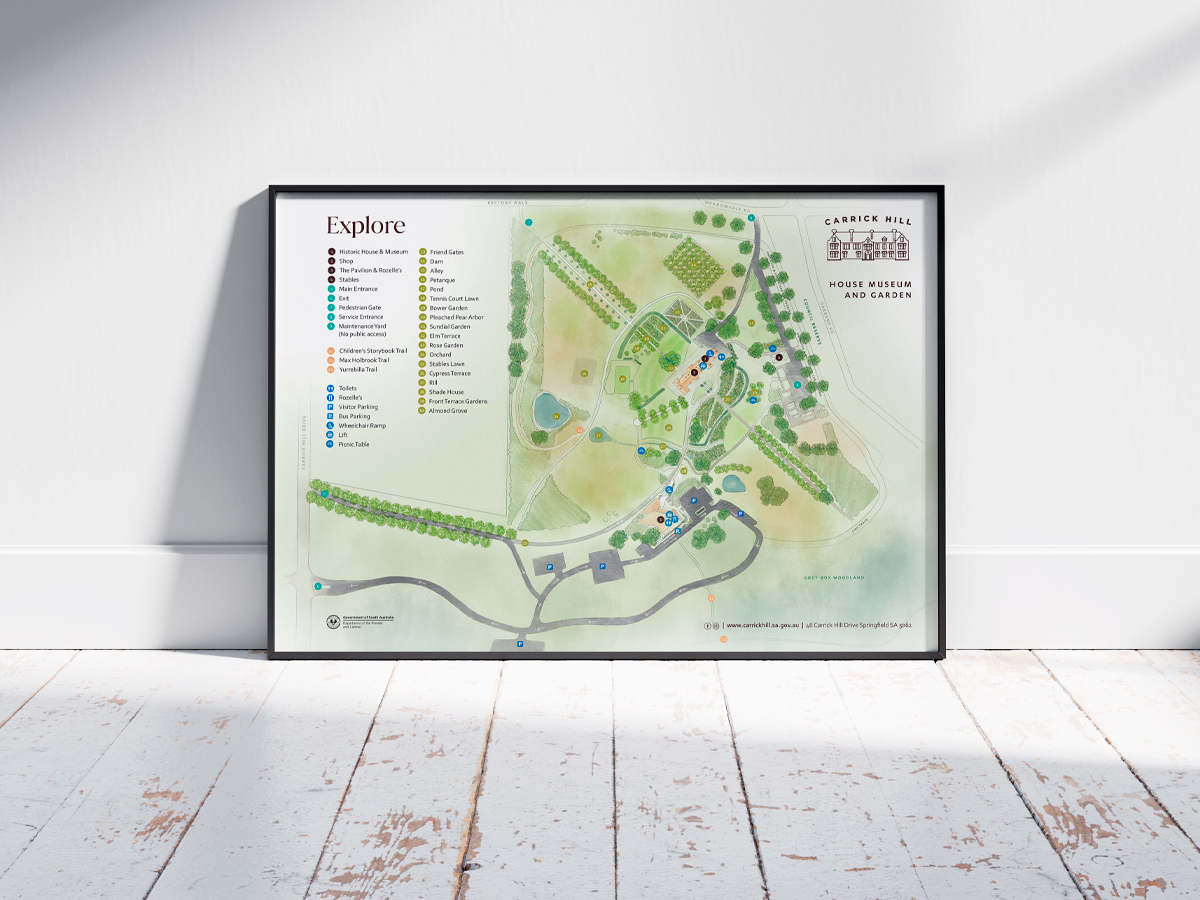 A framed map of Carrick Hill House Museum and Gardens rests on a white wall. The map details various points of interest with a labeled key using colorful dots. It is positioned on a wooden floor with light streaming in and casting shadows.