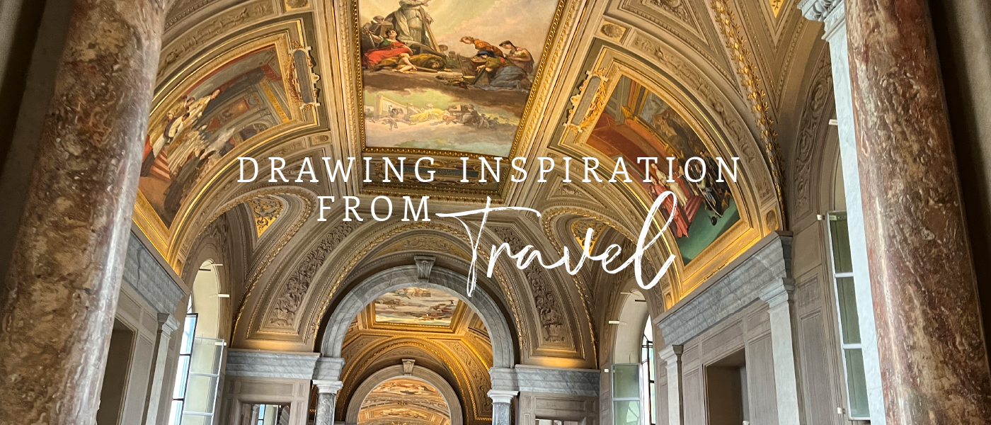 A grand interior view of an ornate hallway with a high, arched ceiling adorned with intricate frescoes. The text overlay reads, "Drawing Inspiration from Travel" in elegant lettering.