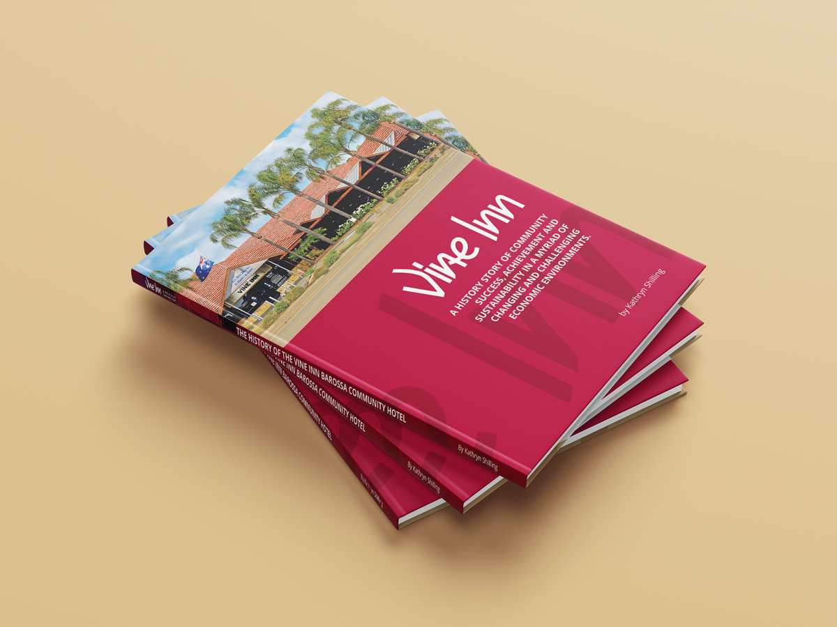 A stack of three copies of a book titled "Vine Inn" with a photo of multi-unit housing on the cover. The background is a soft beige surface, and the book has a red cover with white text detailing the history and development of a housing community.