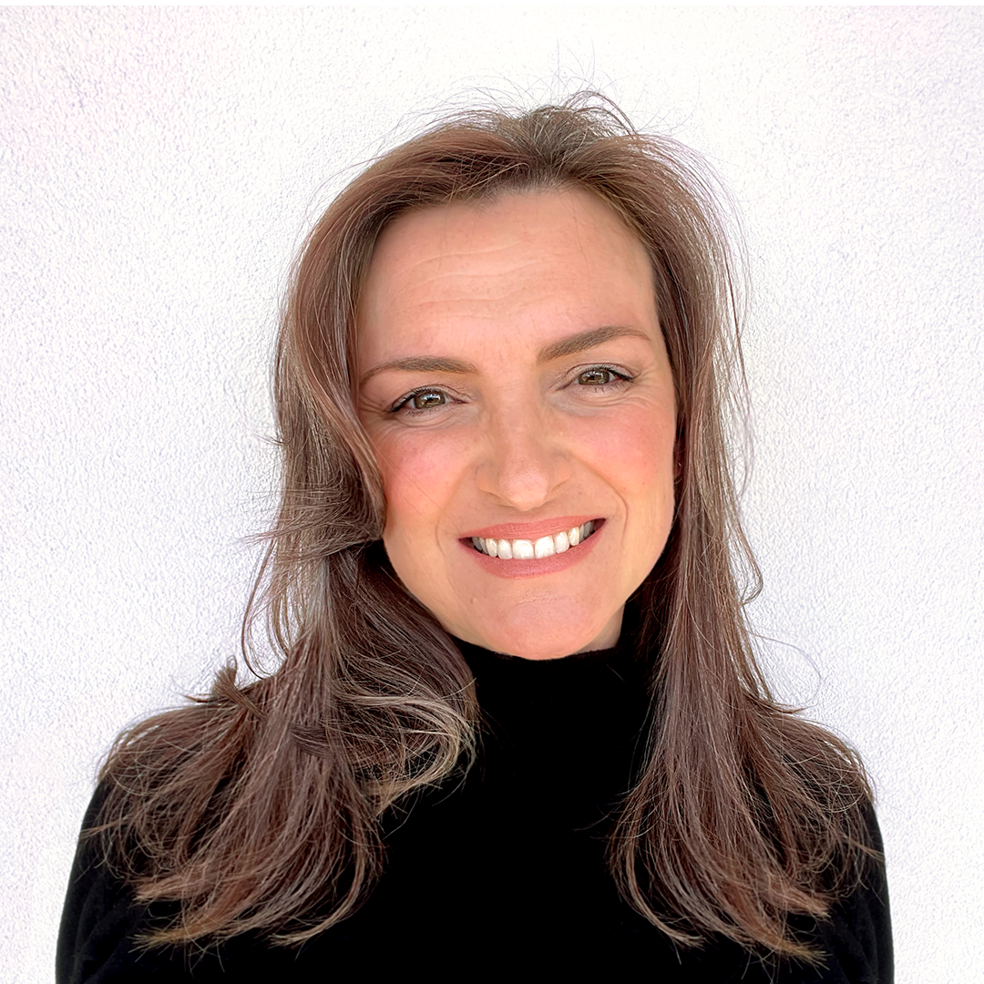 A woman with light brown hair and a black turtleneck smiles in front of a plain white background.